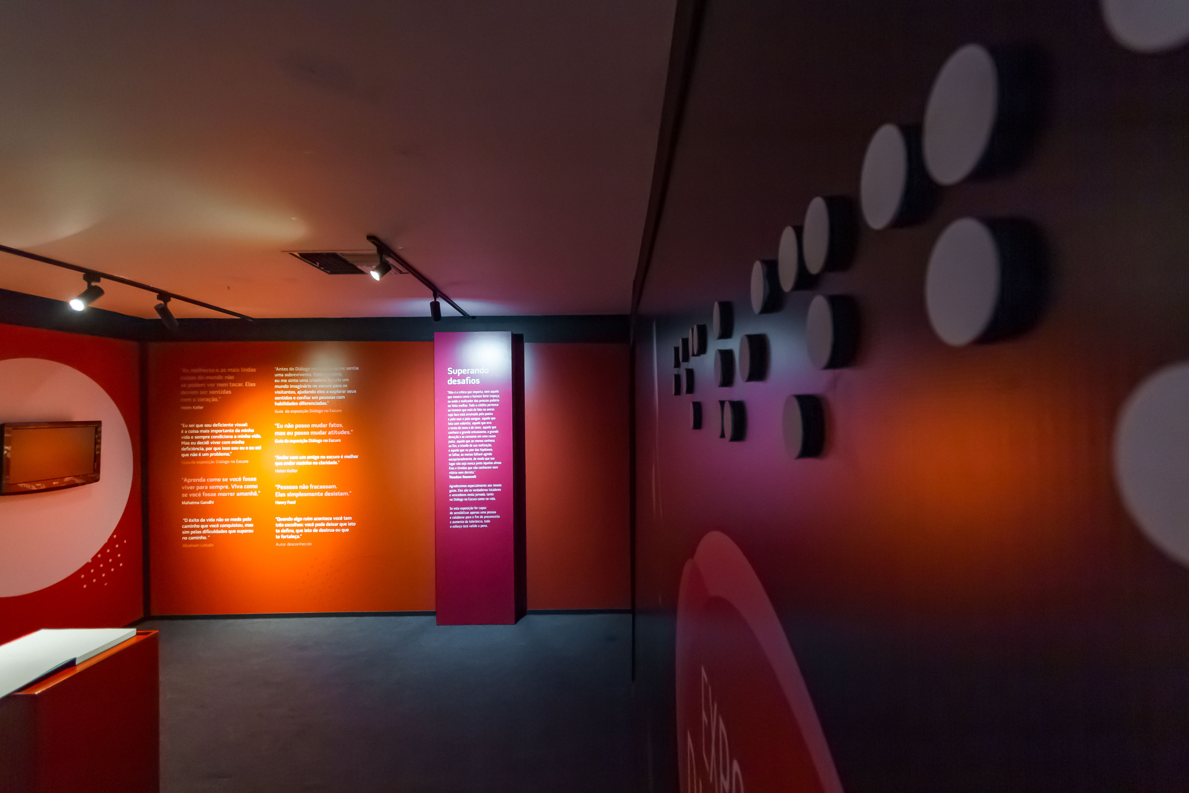 Parede com frases e fundo vermelho, porta de saída da exposição e bem vindo escrito em Braille